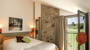 Une chambre d’hôtel avec un lit, un mur en pierre, un balcon avec vue et un tableau accroché au mur.