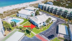 An aerial view of a coastal resort with a swimming pool, multiple buildings, and a beach.