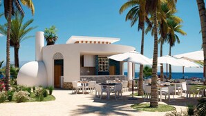 Un restaurante frente al mar con terraza, palmeras y vistas al océano.