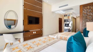 Habitación de hotel con cama, escritorio, televisor y baño visible a través de una puerta abierta.