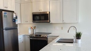 A modern kitchen with white cabinets, stainless steel appliances, and a central island with a sink. - Almost oceanfront Pebble Beach condo, indoor & outdoor pools, 3min to the beach! (Emerald Isle)