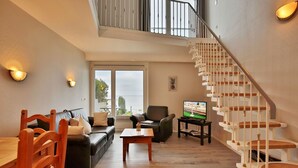 Een ruime woonkamer met een moderne trap, een zithoek, een eettafel en een televisie.