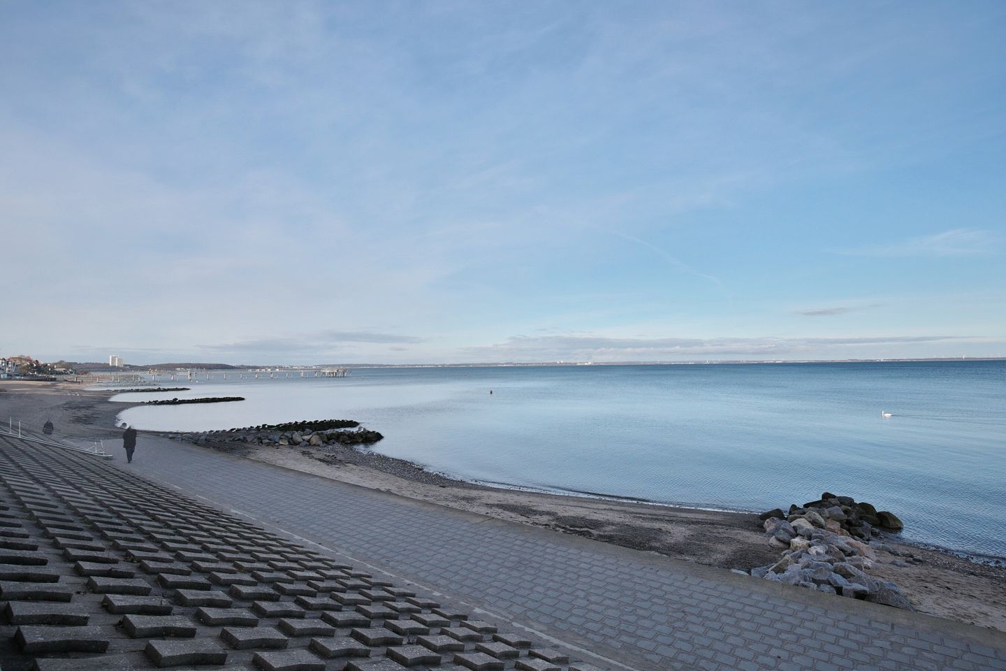 A coastal walkway with a paved path, a sandy beach, and a calm sea.