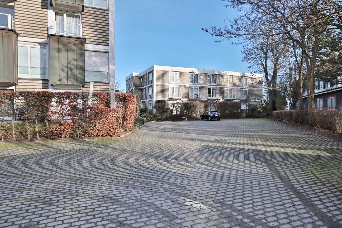 Zona residenziale con cortile lastricato, moderni palazzi a schiera e un'auto parcheggiata in lontananza.