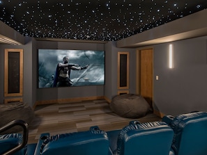 A home theater room with a large screen, blue seating, and a starry ceiling.