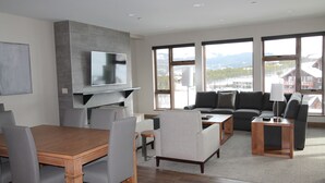 Una sala de estar moderna con una mesa de comedor de madera, sillas tapizadas de color gris, un sofá gris y un televisor de pantalla plana montado en una pared gris.