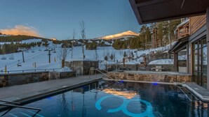 Piscina con vista a la montaña, telesilla y edificio de madera con amplias ventanas.