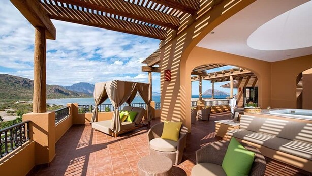 Une terrasse avec coin salon extérieur, un jacuzzi et une vue sur les montagnes et la mer.