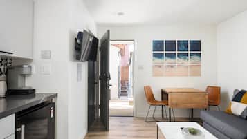 A modern kitchen with a built-in coffee machine, a refrigerator, and a TV mounted on the wall.