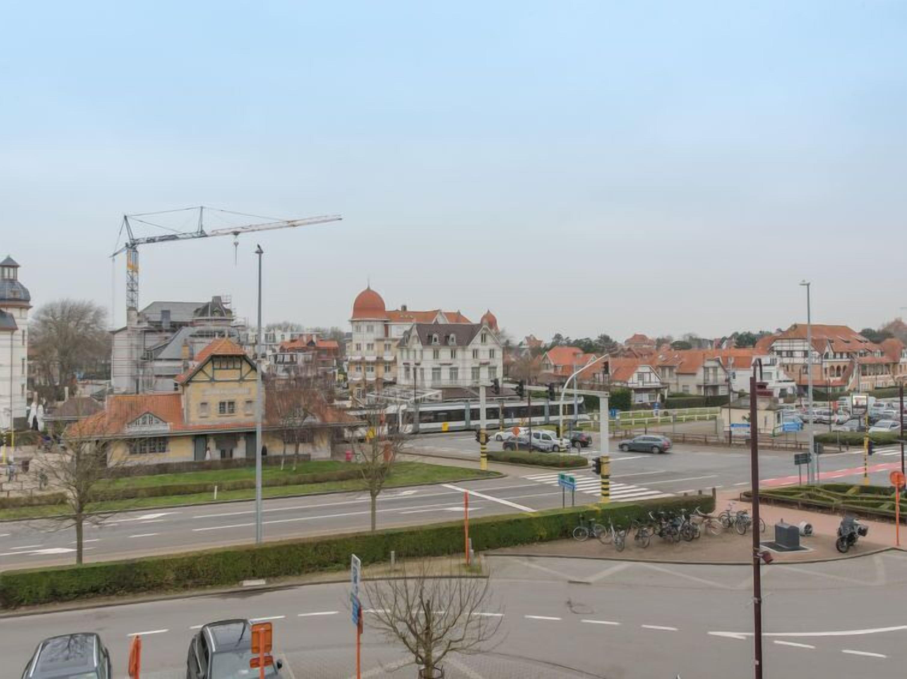 A city intersection with buildings, a tram, and parked cars.