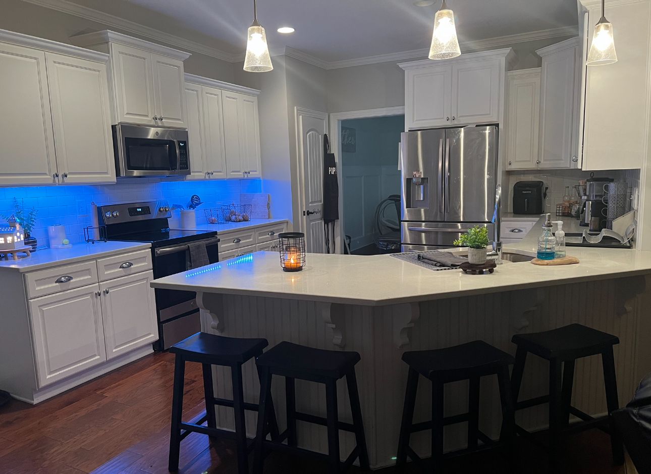 Una cocina moderna con armarios blancos, electrodomésticos de acero inoxidable y una isla central con taburetes de bar.