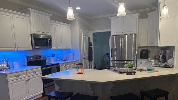Una cocina moderna con armarios blancos, electrodomésticos de acero inoxidable y una isla central con taburetes de bar.