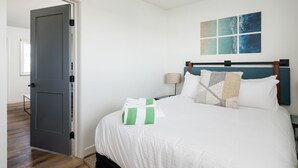 Ein Schlafzimmer mit Bett, Nachttisch, Lampe, Tür und Fenster.