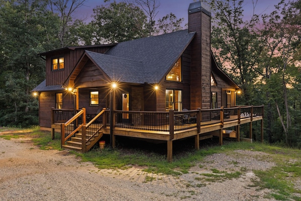 A two-story log cabin with a deck, stairs, and multiple windows.