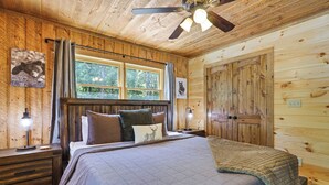 A wooden cabin bedroom with a bed, nightstands, a ceiling fan, and a window.