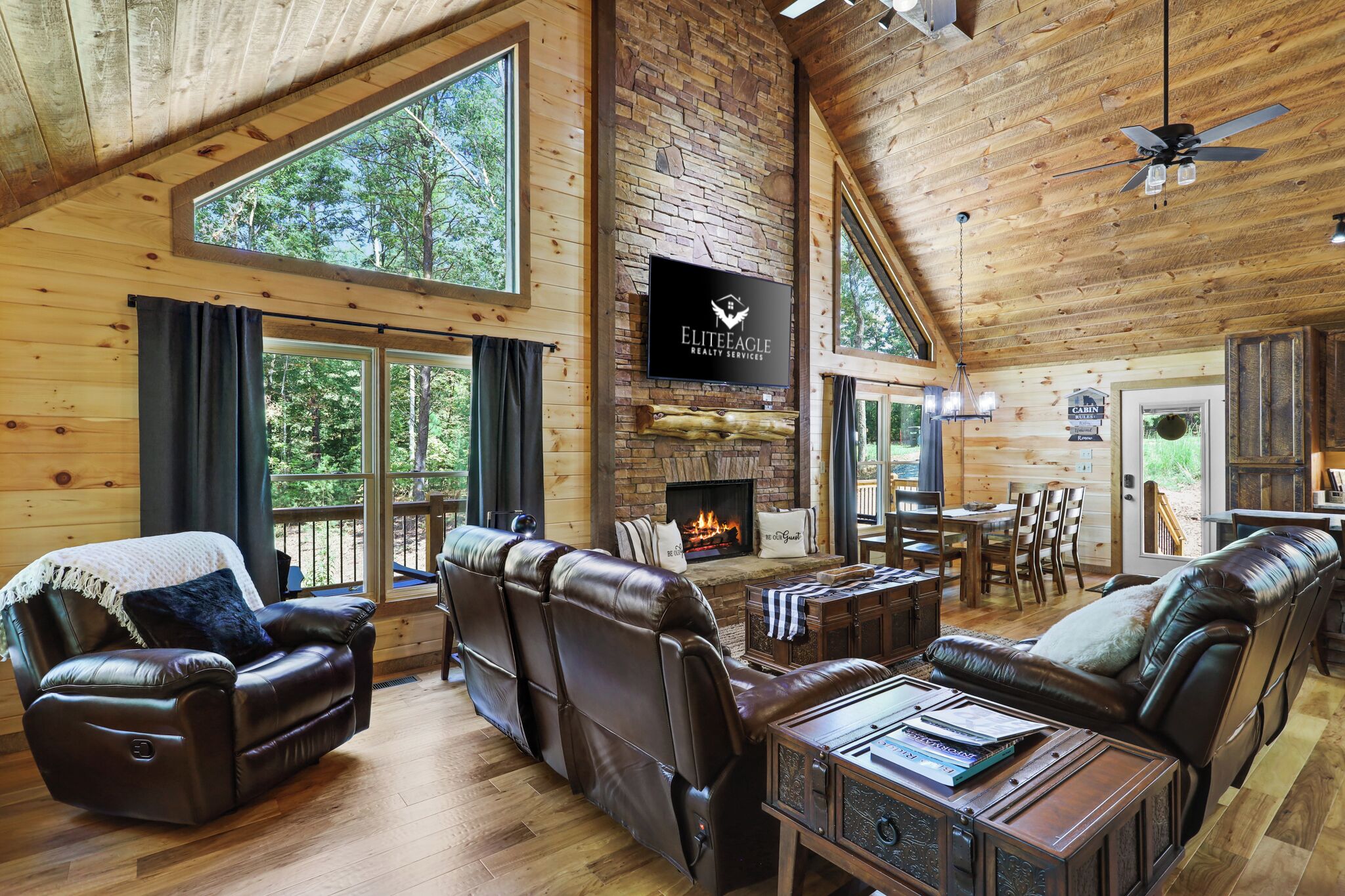 A spacious living area with leather sofas, a fireplace, and a large TV screen displaying 'Elite Eagle Realty Services'.