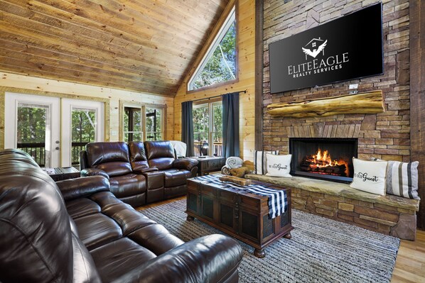 Een gezellige woonkamer met een leren bank, een open haard en een wandtelevisie waarop 'ELITE EAGLE REALTY SERVICES' staat.
