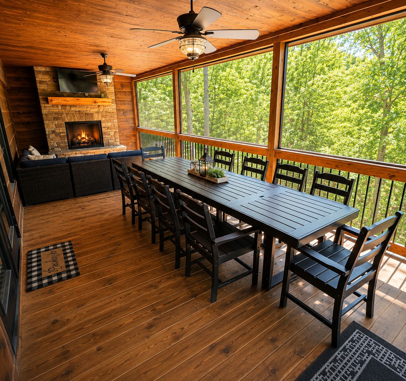 A wooden deck with a dining table and chairs, a fireplace, and a large window overlooking trees.
