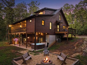 A two-story log cabin with a deck, outdoor seating, and a fire pit.
