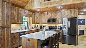 A rustic kitchen with wooden cabinets, a stainless steel refrigerator, a microwave, and a large island with bar stools.