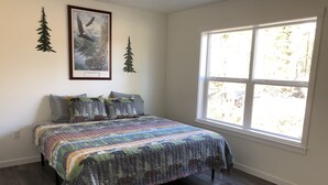 Une chambre avec une grande fenêtre, un lit recouvert d’une couette aux couleurs vives, et deux éléments décoratifs fixés au mur.