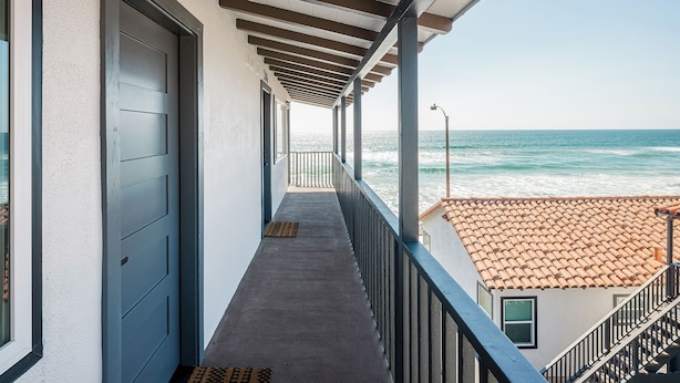 A balcony with a view of the ocean, a door labeled '305', and a tiled roof in the background.