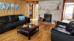 A cozy living room with a fireplace, wooden walls, and a leather sofa. - Beautiful Lake House for Rent (Neebing)