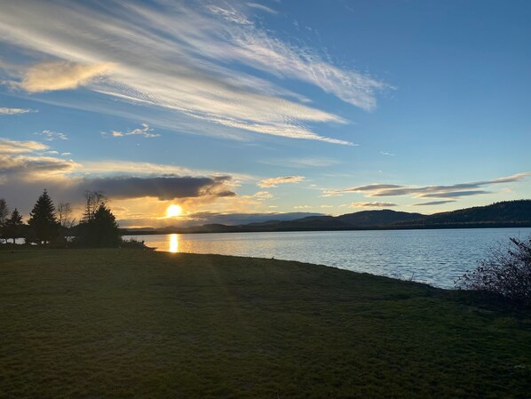 A lakeside view with a sunset, trees, and distant hills.