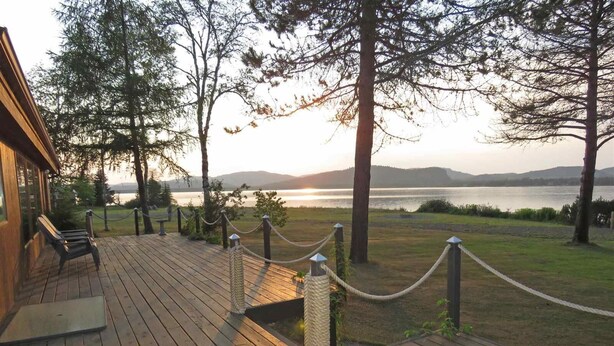 A wooden deck with a bench, a rope barrier, and a view of a lake and mountains. - Beautiful Lake House for Rent (Neebing)