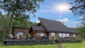 A wooden cabin with a deck, surrounded by a grassy area and trees. - Beautiful Lake House for Rent (Neebing)