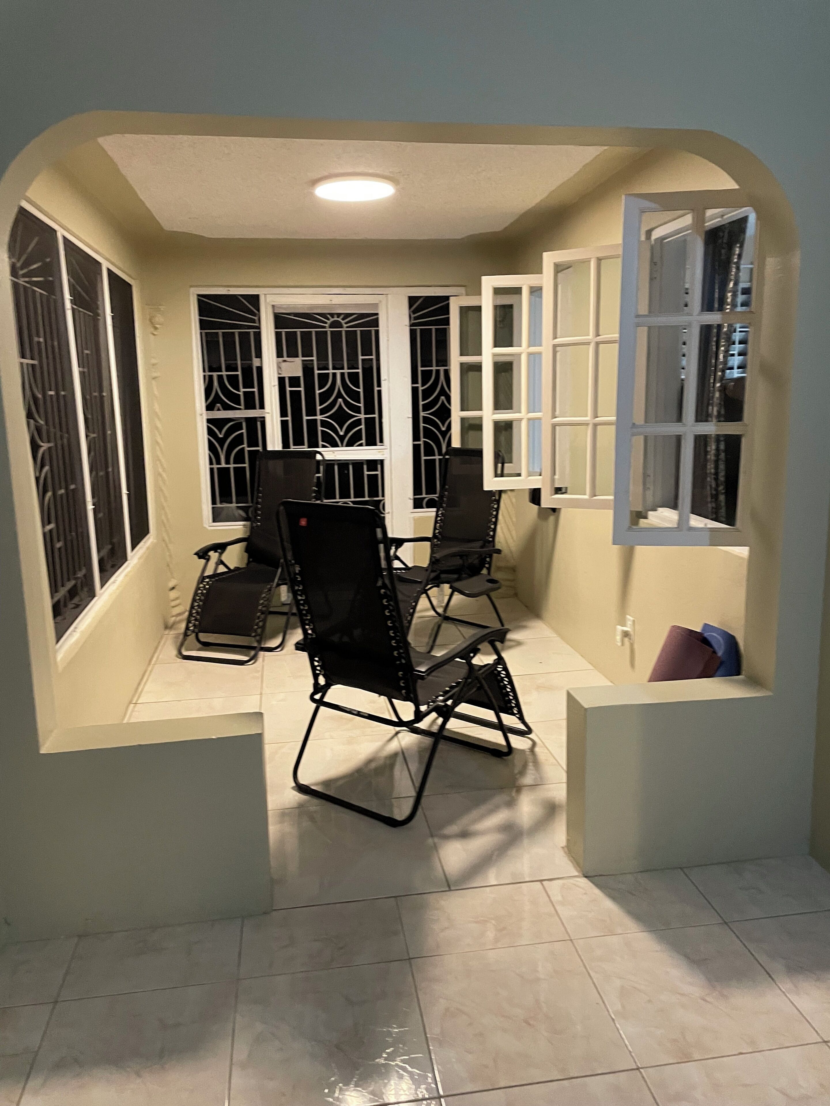 Une pièce avec un sol carrelé, une table entourée de chaises, des fenêtres grillagées et une porte.