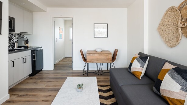 Una sala de estar moderna con un sofá gris, una mesa de centro y un comedor con una mesa de madera y sillas.