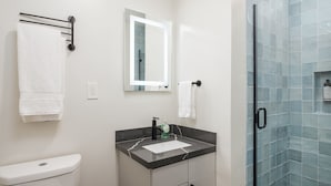 Un baño moderno con inodoro, lavabo, espejo y cabina de ducha de vidrio.