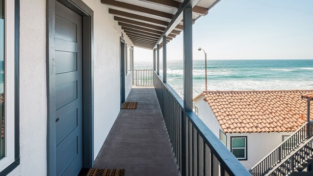 Un balcon avec vue sur l’océan, une porte portant l’inscription « 305 », et un toit recouvert de tuiles en arrière-plan.