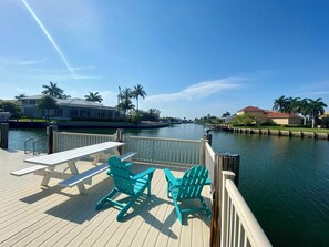 Enjoy a serene waterfront setting with a deck, picnic table, and Adirondack chairs overlooking a calm body of water.