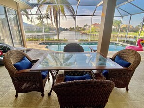 Relax by the pool with a view of the surrounding neighborhood from this patio area, featuring a glass-top table and comfortable wicker chairs.