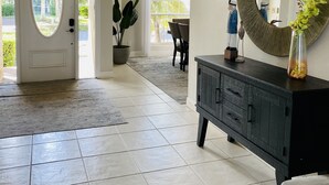 A spacious foyer with a large door, a dark wooden console, and a round mirror. - 8 Minute Walk to Beach Luxury 4 Bdrm Waterfront home -salt water heated Pool (Marco Island)