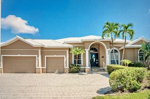 A two-story house with a beige facade, a front entrance with a glass door, and a driveway leading to a garage.