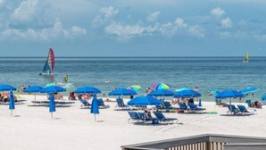 A beach with sun loungers and umbrellas, a sailboat, and a clear sky. - 8 Minute Walk to Beach Luxury 4 Bdrm Waterfront home -salt water heated Pool (Marco Island)