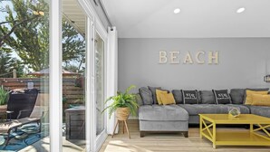 A modern living room with a grey sofa, yellow coffee table, and a large window overlooking a backyard. - Luxurious Private Pool | Beach Walk with Private Access 🏖️✨ (Miramar Beach)