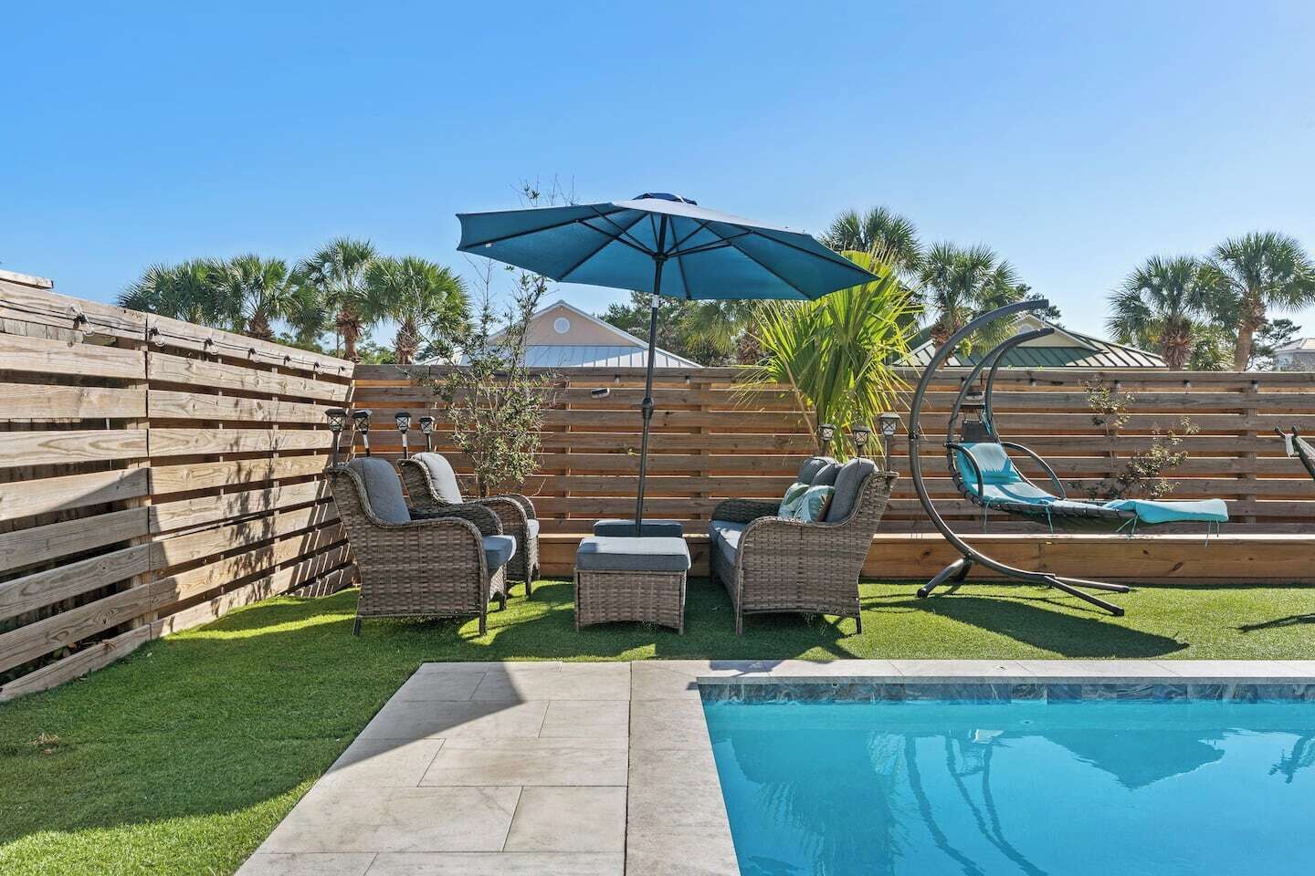 Un jardin avec une piscine, une clôture en bois, des meubles en osier et une chaise suspendue.