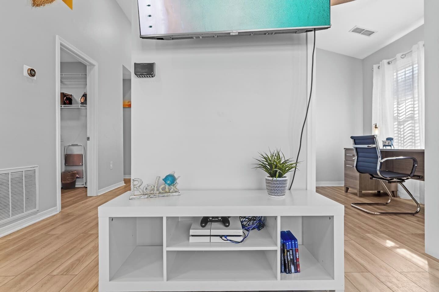 A modern living room with a white entertainment unit, a flat-screen TV, a potted plant, and a desk with a chair.
