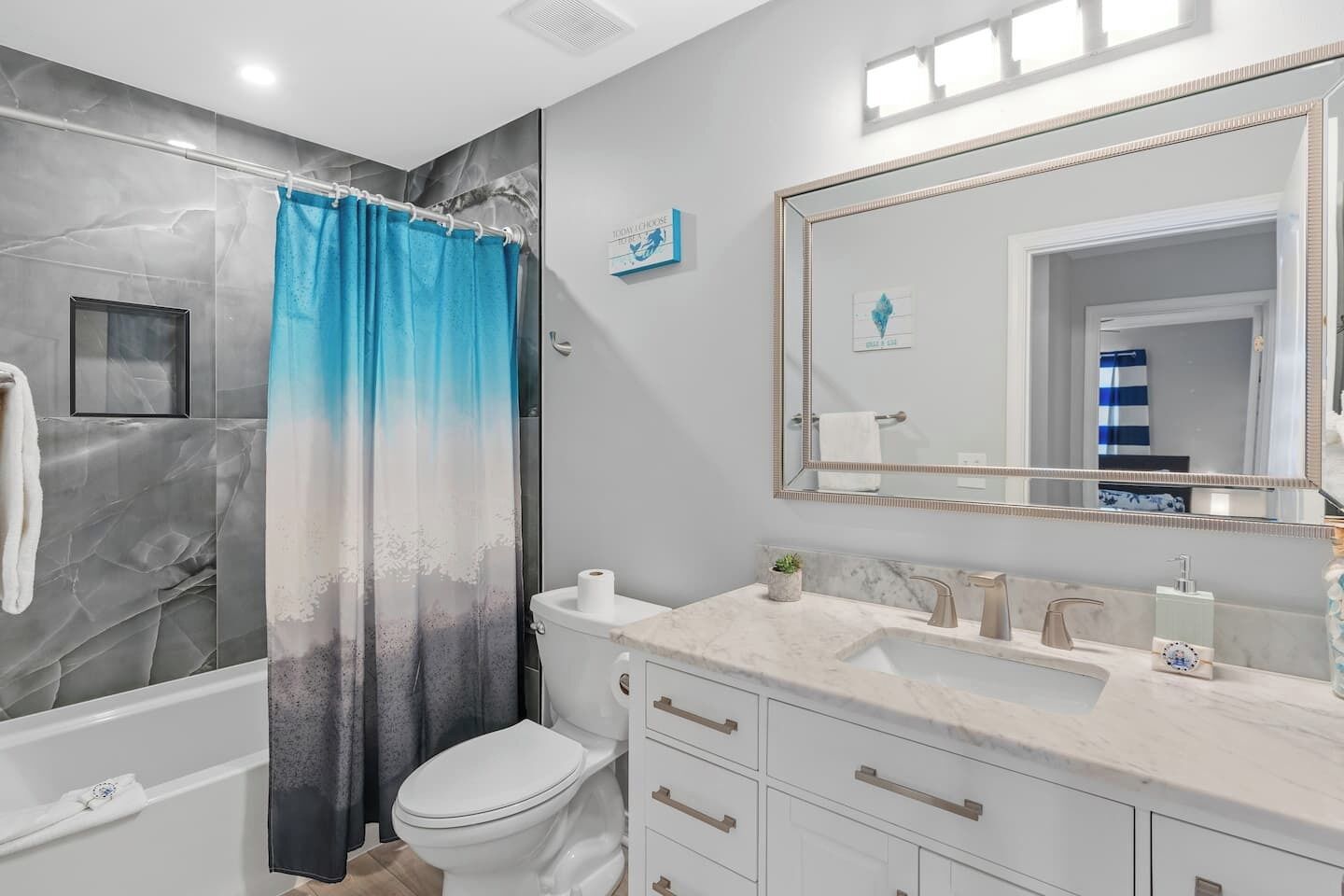 A modern bathroom with a marble shower, a toilet, a sink with a marble countertop, and a large mirror.