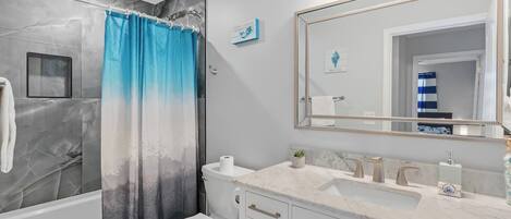 A modern bathroom with a marble shower, a toilet, a sink with a marble countertop, and a large mirror.