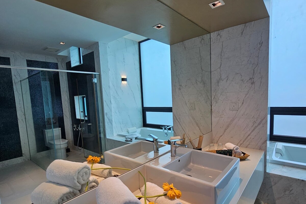 A modern bathroom with a large mirror, two sinks, and a bathtub. There are towels and flowers on the counter.