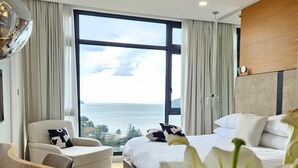 Habitación de hotel moderna con una cama grande, una zona de estar con una mesa y vistas al mar.