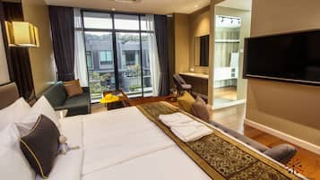 A hotel room with a large bed, a sofa, a desk, and a TV. There is a view of the outside through the window.