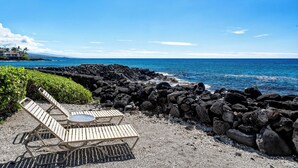 Una spiaggia con sdraio e un tavolo, costa rocciosa e vista sull'oceano.