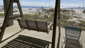 Ein hölzerner Schaukelstuhl, befestigt an einem Metallgestell, mit Blick auf einen sandigen Strand und vereinzelter Vegetation.