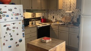 Eine kompakte Küche mit Kühlschrank, Herd und Spüle. In der Mitte steht ein kleiner Holztisch.